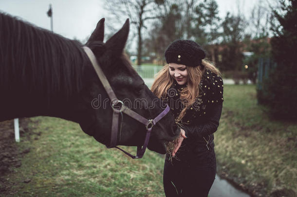 美丽的金发女孩从一只手中喂养一匹棕色的大马