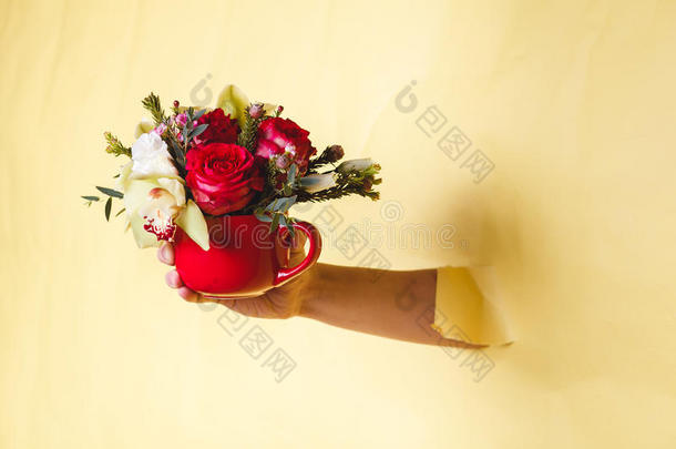 手拿着带花的小花瓶，玫瑰在黄色的背景下折断