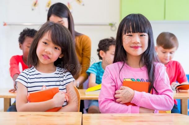 两个亚洲人女孩小孩热烈地拥抱书和微笑的采用教室和whiteiron白铁