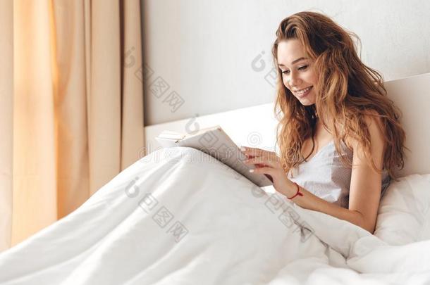 欢乐的漂亮的女士谎言向床在室内阅读书.