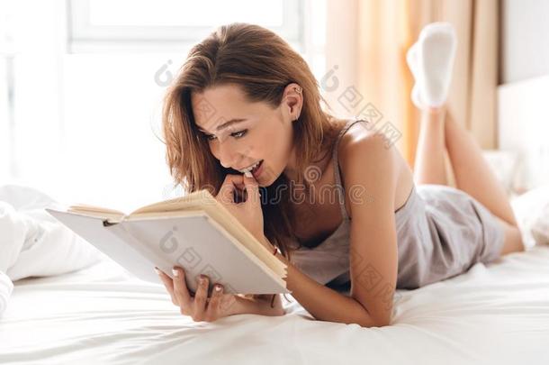 欢乐的漂亮的女士谎言向床在室内阅读书.