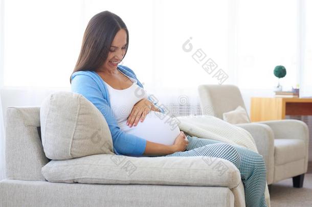幸福的怀孕的女人静止的在家向指已提到的人沙发