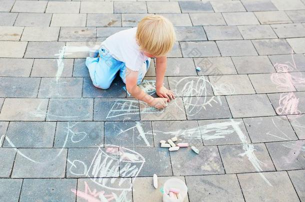 小的男孩绘画和制造白色或彩色粉笔的白垩向沥青