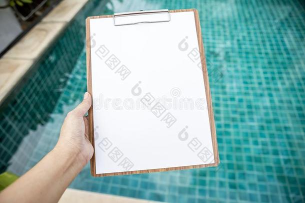 空白的白色的纸向木制的有纸夹的笔记板越过变模糊游泳水池
