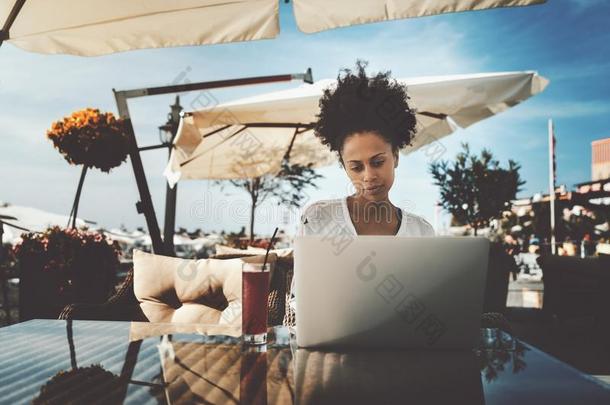 非洲式发型有卷发的女孩和便携式电脑采用大街咖啡馆
