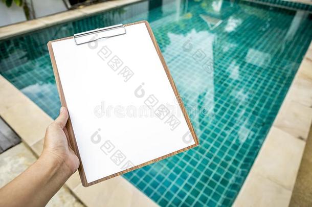 空白的白色的纸向有纸夹的笔记板越过清楚的水游泳水池波黑
