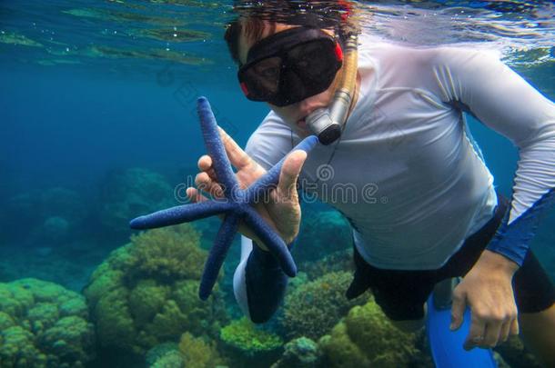 男人用通气管潜泳采用蓝色水和星鱼.Snorkel采用g采用珊瑚