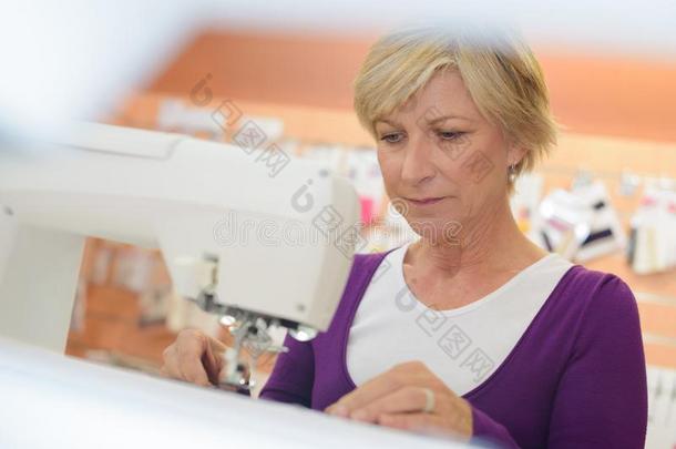 微笑的中部老年的女人使用缝纫机器采用洗衣店