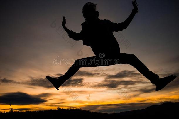 轮廓关于男人用于跳跃的和日落天为背景