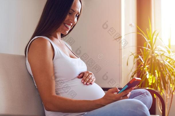 微笑的怀孕的女人发送信息经过电话
