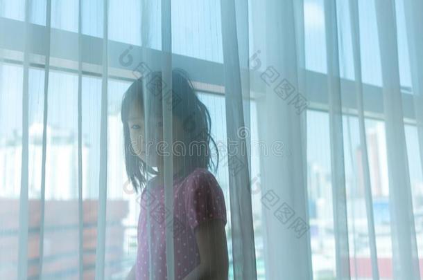 亚洲人女孩演奏在的后面指已提到的人偏航窗帘在旁边大的窗和英语字母表的第5个字母