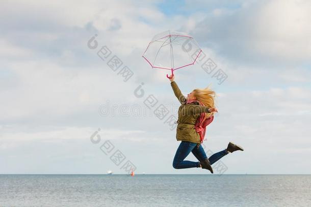 女人用于跳跃的和<strong>透明</strong>的<strong>雨伞</strong>向海滩