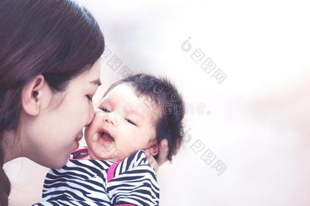 年幼的亚洲人母亲热烈地拥抱和接吻的她新生的婴儿女孩