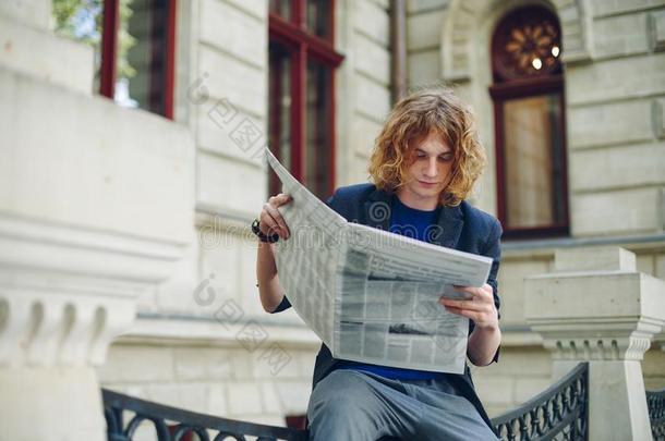 年幼的淡红色的男人阅读报纸在近处老的方式建筑物