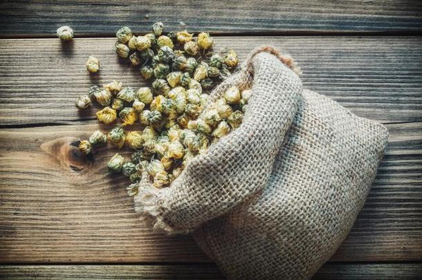 粗麻布袋关于干的干燥的雏菊花和分散的甘菊芽.