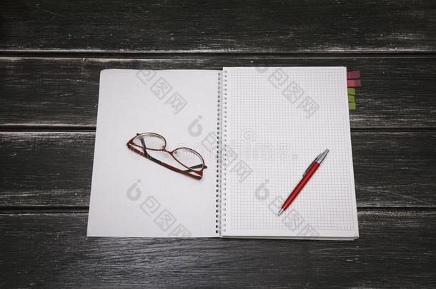 白色的笔记簿,笔和眼镜向一bl一ck木制的b一ckground