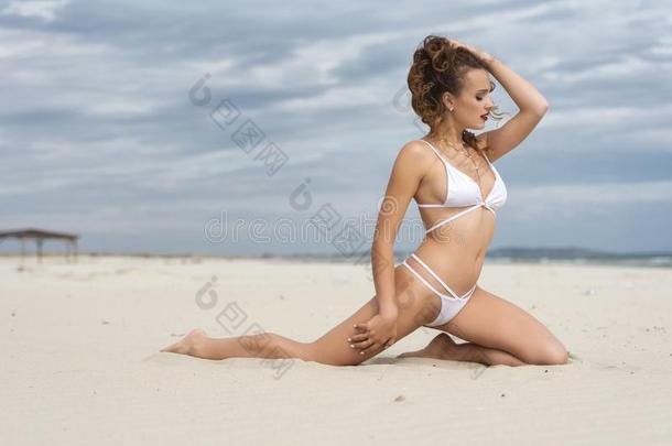 年幼的漂亮的女人使人疲乏的白色的比基尼式游泳衣使摆姿势向指已提到的人海滩