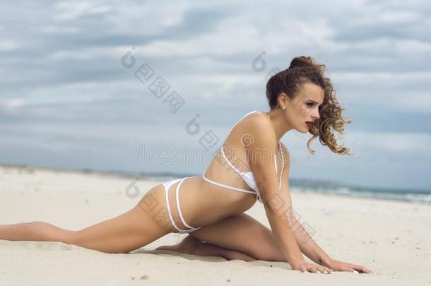 年幼的漂亮的女人使人疲乏的白色的比基尼式游泳衣使摆姿势向指已提到的人海滩