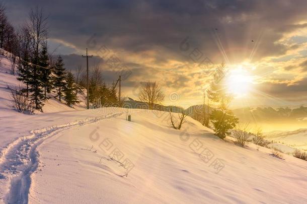 乡下的人行道通过下雪的山坡在日落