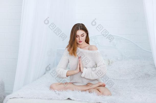 一女孩坐采用一莲花使摆姿势和关闭着的眼睛向一床向一白色的