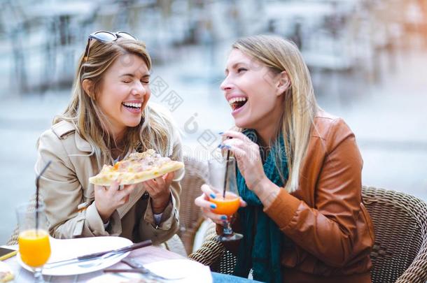 肖像关于两个年幼的女人吃意大利薄饼在户外