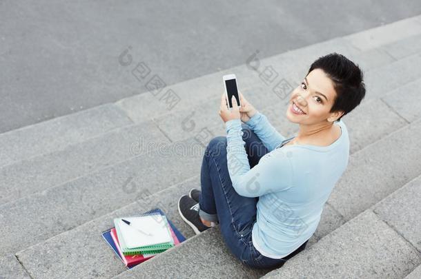 微笑的年幼的女人使用智能手机在户外