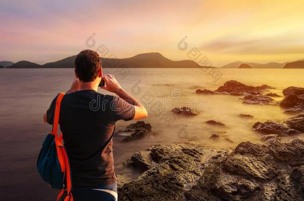 男人使用智能手机射击影像向海日落或日出采用