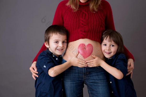 美丽的未满学龄的孩子们,热烈地拥抱他们的怀孕的妈妈