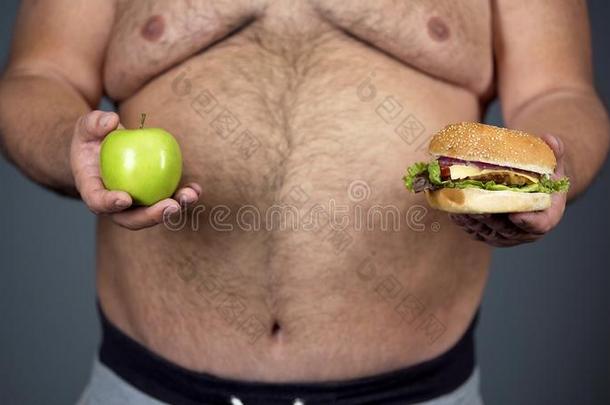 肥的男人挑选在之间苹果和汉堡包,遵守向健康的