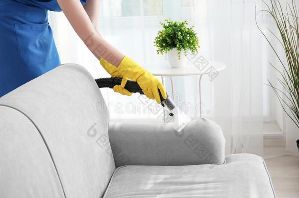 女人清洁长沙发椅和真空清洁剂