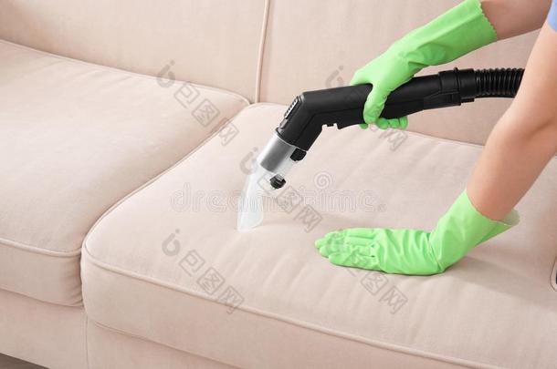 女人清洁长沙发椅和真空清洁剂