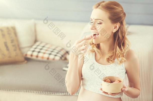 积极的高兴的怀孕的女人吃马卡龙在家