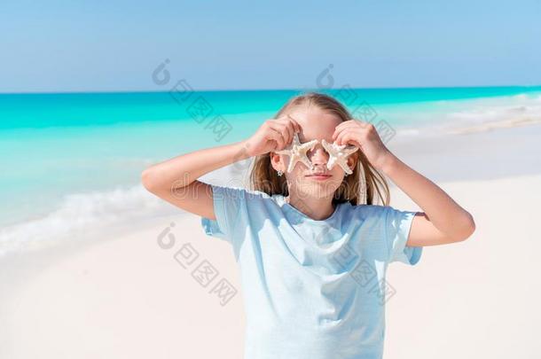 值得崇拜的小的女孩和海星向白色的空的海滩