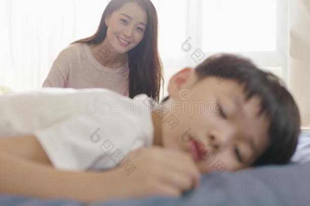 微笑的亚洲人母亲有样子的在他的儿子采用睡采用指已提到的人morn采用g