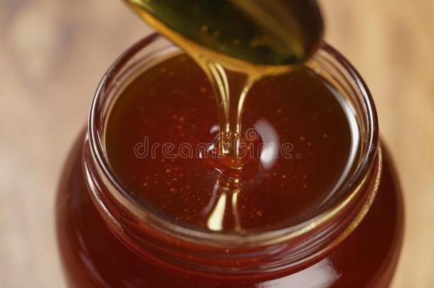 传布有机的蜂蜜从勺进入中玻璃罐子
