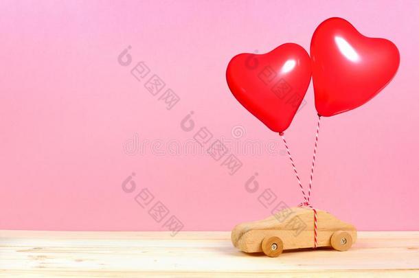 木制的汽车和红色的心气球反对粉红色的背景