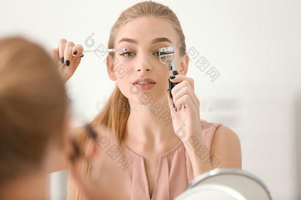 美丽的年幼的女人使用睫毛刷子
