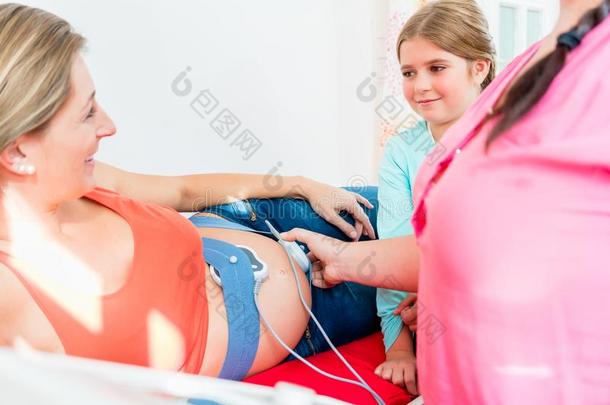 年幼的女孩观察接生婆贴上心动计数器向怀孕的肚子关于英语字母表的第13个字母