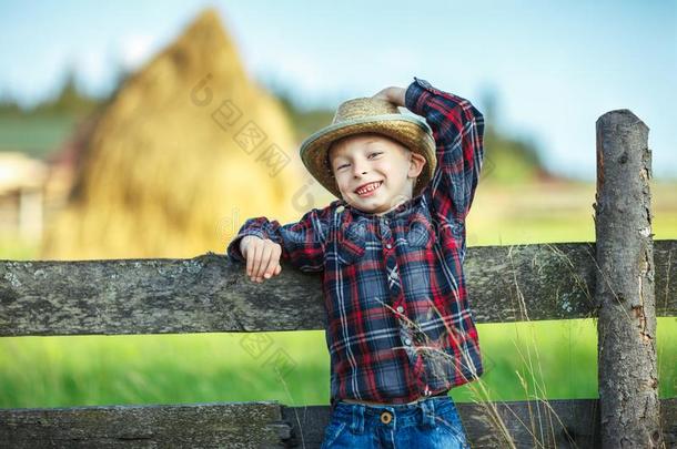 小的男孩坐向木制的栅栏反对美丽的干草堆