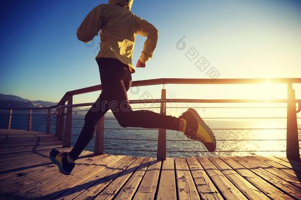 慢跑锻炼者早晨练习向海滨用木板铺成的小道在的时候日出