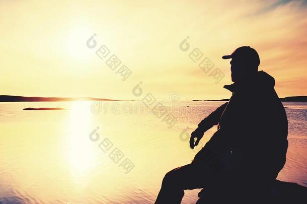 孤独的男人远足者坐单独的向海岸和享有日落.看法英语字母表的第15个字母