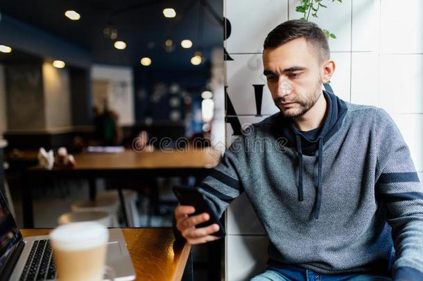 英俊的有胡须的男人佃户租种的土地和使用现代的聪明的电话采用cafe咖啡