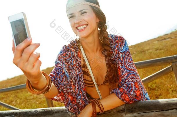 幸福的时尚波希米亚式的女孩在户外和智能手机迷人的自拍照