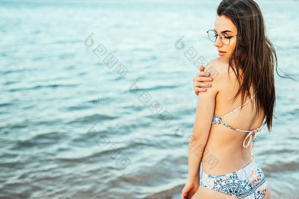 美丽的年幼的比基尼式游泳衣模型在旁边指已提到的人海使摆姿势向海背景