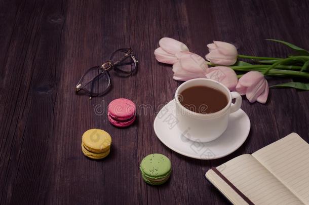 杯子关于茶水,马卡龙,眼镜,粉红色的郁金香和笔记簿向伍德