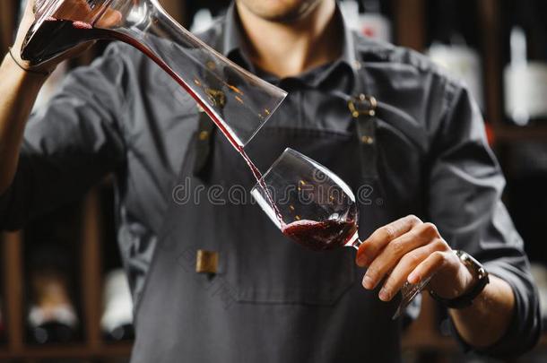 酒吧间销售酒精饮料的人涌出红色的葡萄酒采用玻璃从大的透明的容器