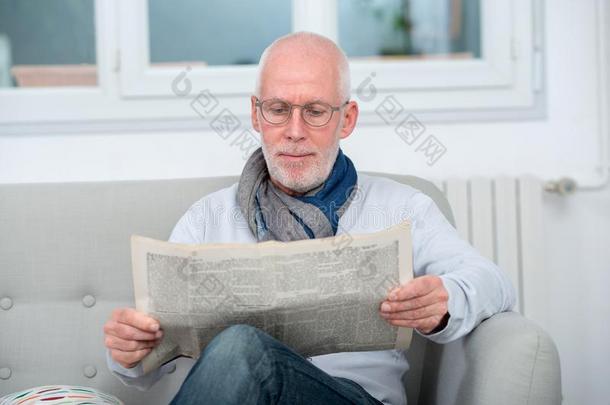 英俊的成熟的男人阅读新报纸向沙发