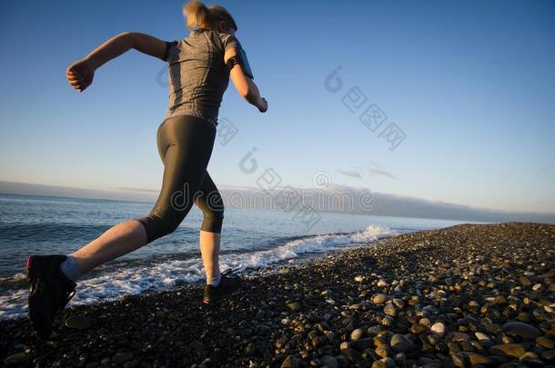 成熟的女人赛跑者跑步向日出海滨.健康的生活方式