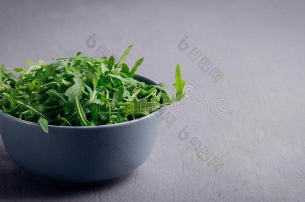 新鲜的绿色的芝麻菜采用碗向灰色的st向e背景.芝麻菜是（be的三单形式