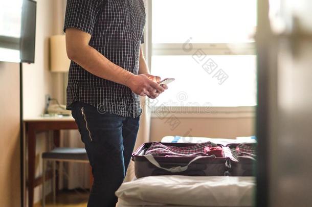 男人使用智能手机采用旅馆房间和敞开的行李